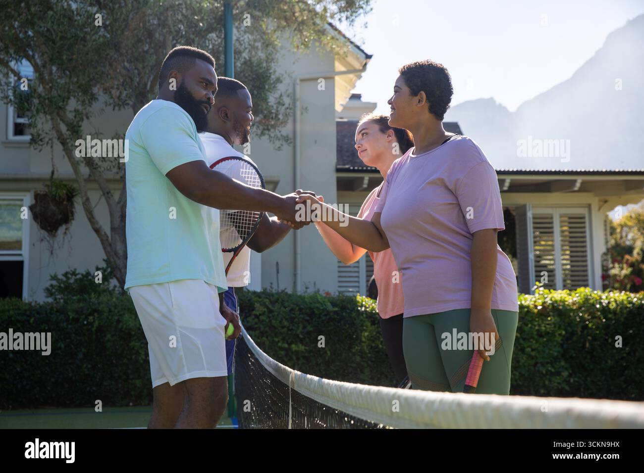Divers joueurs de tennis serrant la main sur un court de banlieue à travers un filet blanc, tenant des raquettes et une balle Banque D'Images
