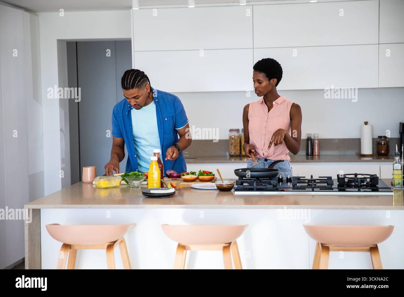 Couple diversifié hacher des légumes sur une planche à découper et cuisiner avec une poêle à frire sur l'îlot de cuisine Banque D'Images Couple diversifié hacher des légumes sur une planche à découper et cuisiner avec une poêle à frire sur l'îlot de cuisine Banque D'Images