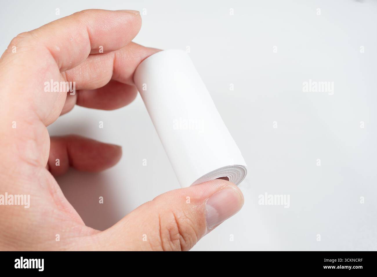 Main tenant un rouleau de papier thermique, symbolisant le contact direct de la peau avec le revêtement chimique du papier, qui peut contenir du BPA (bisphénol A) Banque D'Images