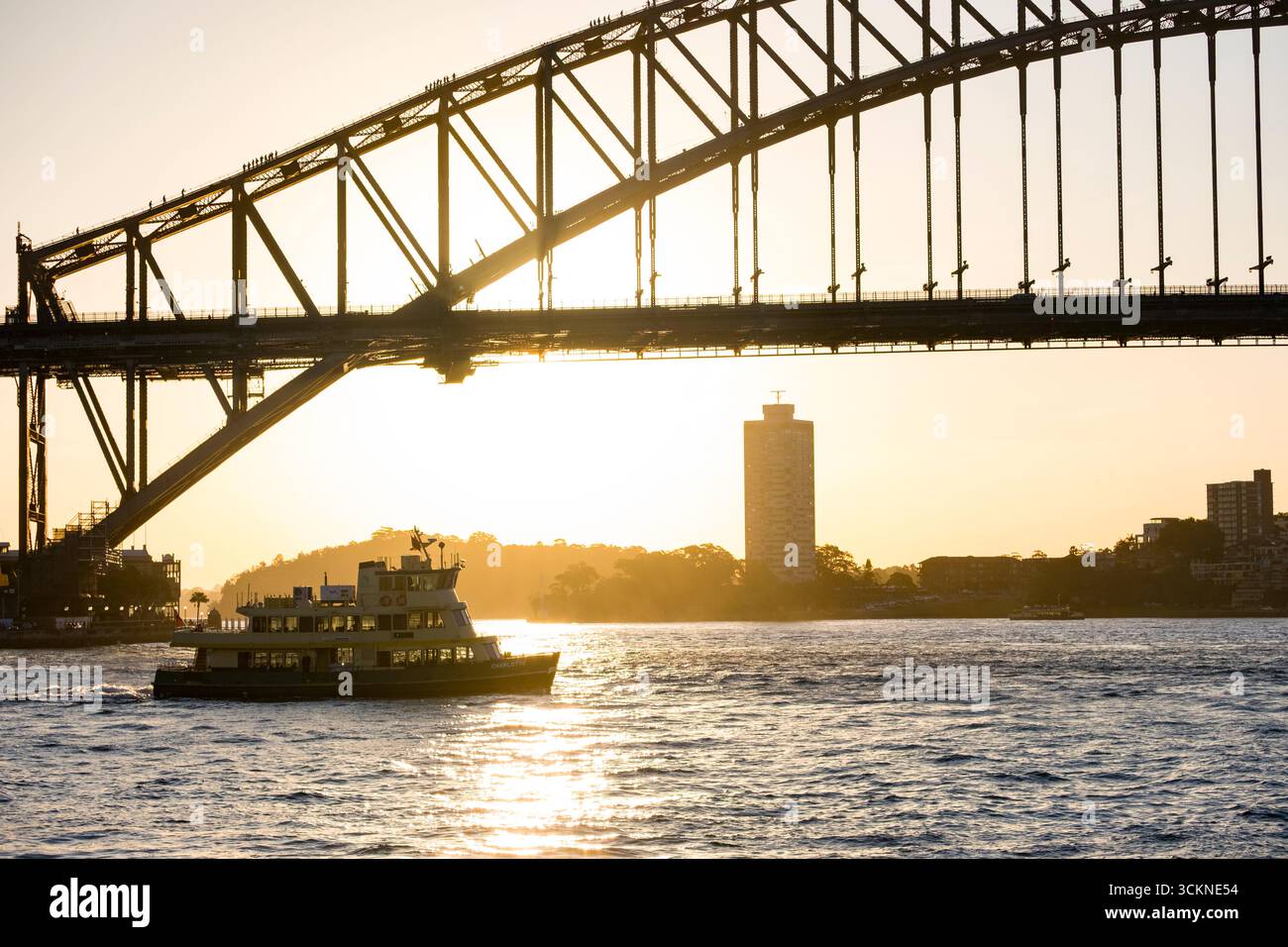 La scène du soir capture une croisière en ferry sous un célèbre pont voûté au coucher du soleil, entouré par des eaux calmes remplies de reflets. Un grand bâtiment A. Banque D'Images