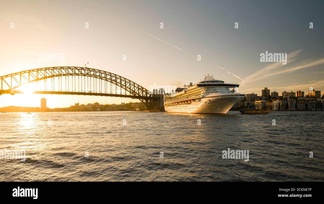 Un bateau de croisière de luxe se déplaçant dans les eaux près du Harbour Bridge de Sydney au coucher du soleil, avec les gratte-ciel environnants baignés d'un glo doré chaud Banque D'Images
