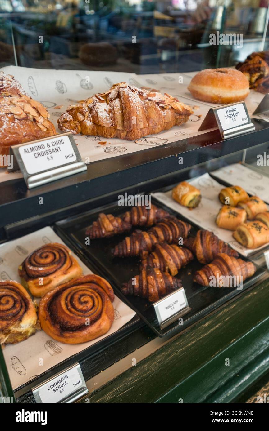Un délicieux assortiment de pâtisseries et de produits de boulangerie, y compris des croissants et des petits pains à la cannelle, présentés dans une vitrine de boulangerie. Une alléchante et v Banque D'Images