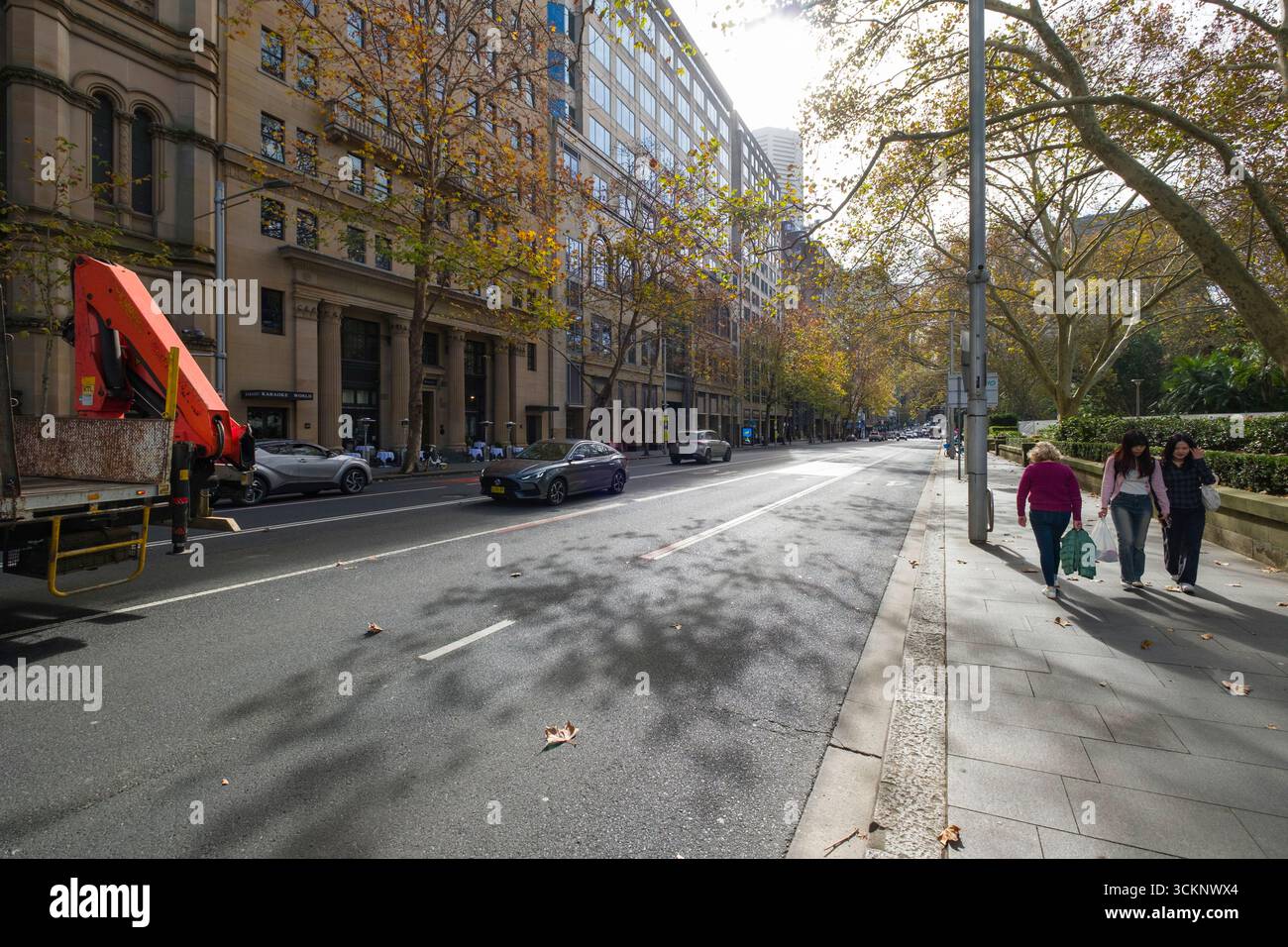 Scène urbaine avec des piétons sur un trottoir de la ville, des arbres d'automne bordant la rue, et la circulation qui passe, avec un mélange d'histoire et de contemporain Banque D'Images