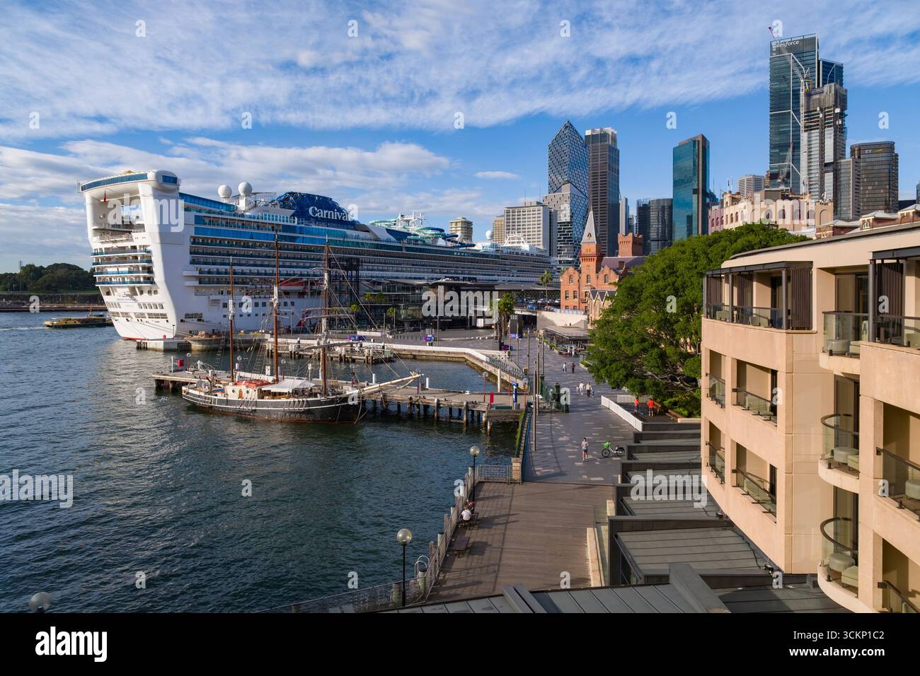 Une vue impressionnante sur le port de Sydney avec un bateau de croisière Carnival Adventure amarré, des bâtiments historiques et des gratte-ciels dynamiques sous un ciel vibrant, Banque D'Images