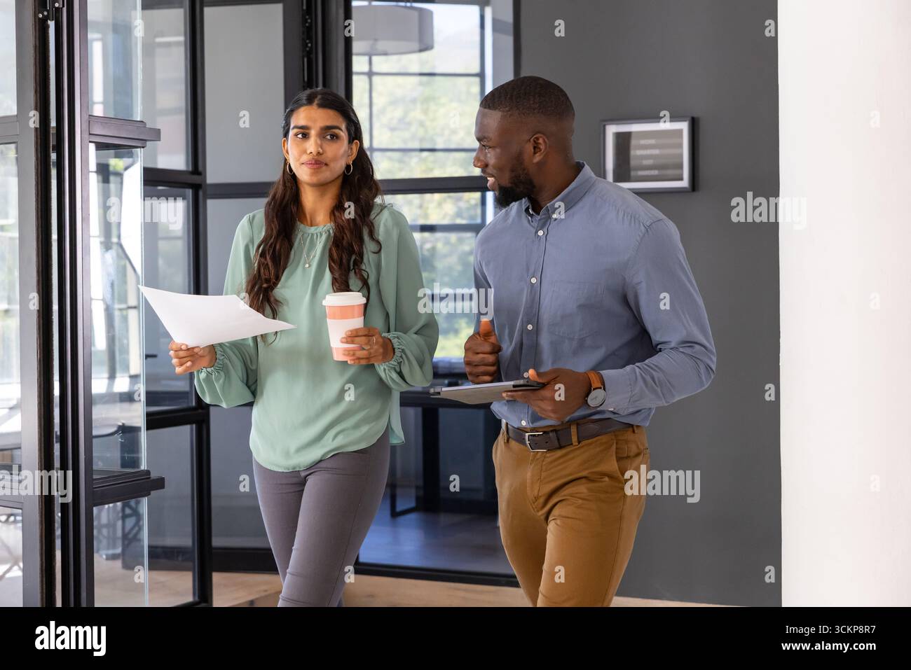 Divers collègues passant la poignée de porte en verre dans le couloir de bureau tenant des papiers tasse à café, tablette Banque D'Images