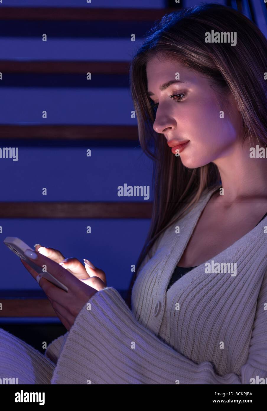 Jeune femme en tapant de profil sur smartphone dans les escaliers. Néon bleu. Banque D'Images