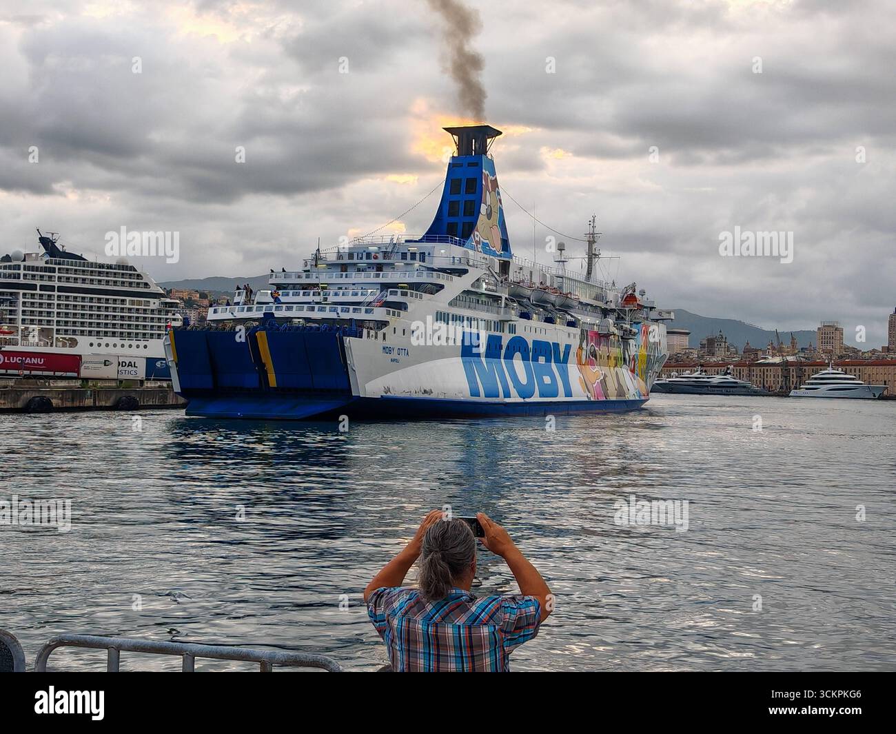 Gênes, Italie - 13 septembre 2025 : un touriste prend une photo du ferry Moby Otta au départ du port de Gênes. Le navire à passagers et RoRo exploité par la compagnie maritime MOBY relie les villes portuaires de la Méditerranée et transporte des véhicules *** Ein Tourist fotografiert die Autofähre Moby Otta BEI der Abfahrt aus dem Hafen von Genua. DAS Passagier- und RoRo-Schiff der Reederei Moby verbindet Hafenstädte im Mittelmeer und transportiert Fahrzeuge Banque D'Images