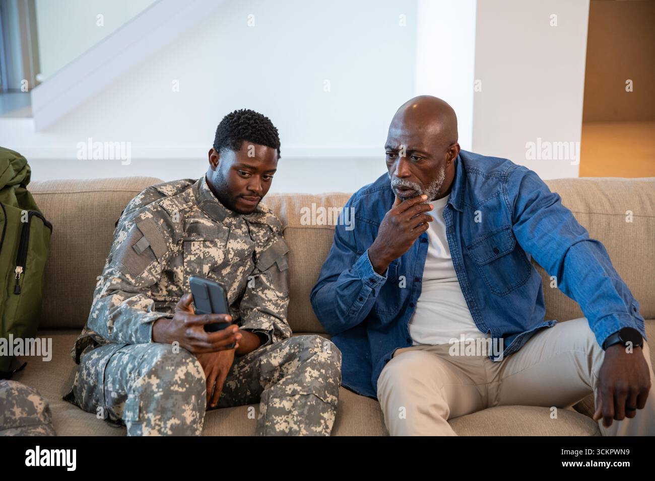 Père soldat afro-américain et fils sur le canapé à la maison explorant smartphone Banque D'Images
