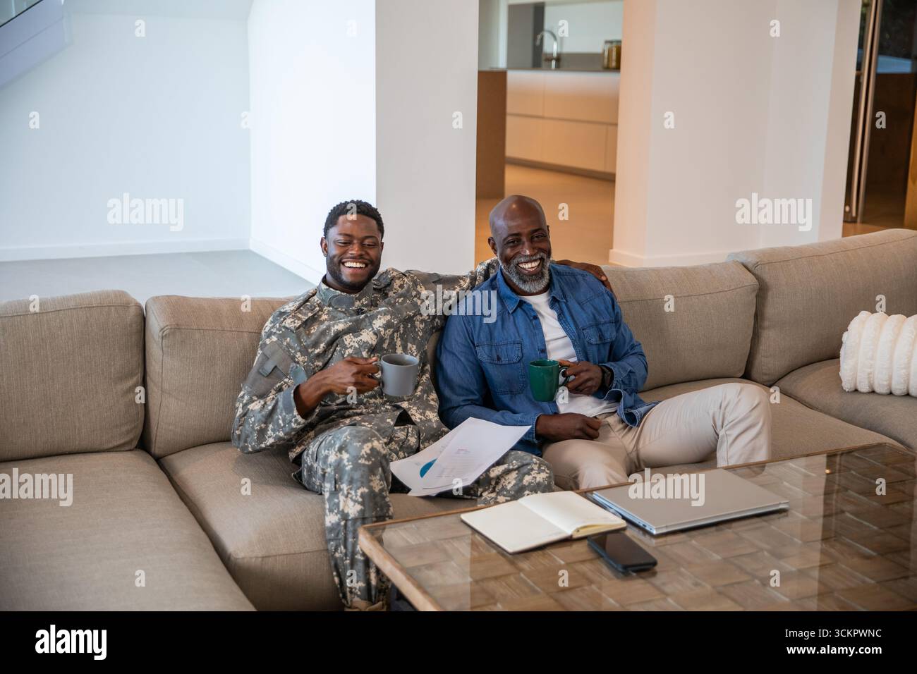 Père afro-américain senior et son fils assis sur le canapé à la maison avec des tasses à café examinant les papiers Banque D'Images Père afro-américain senior et son fils assis sur le canapé à la maison avec des tasses à café examinant les papiers Banque D'Images