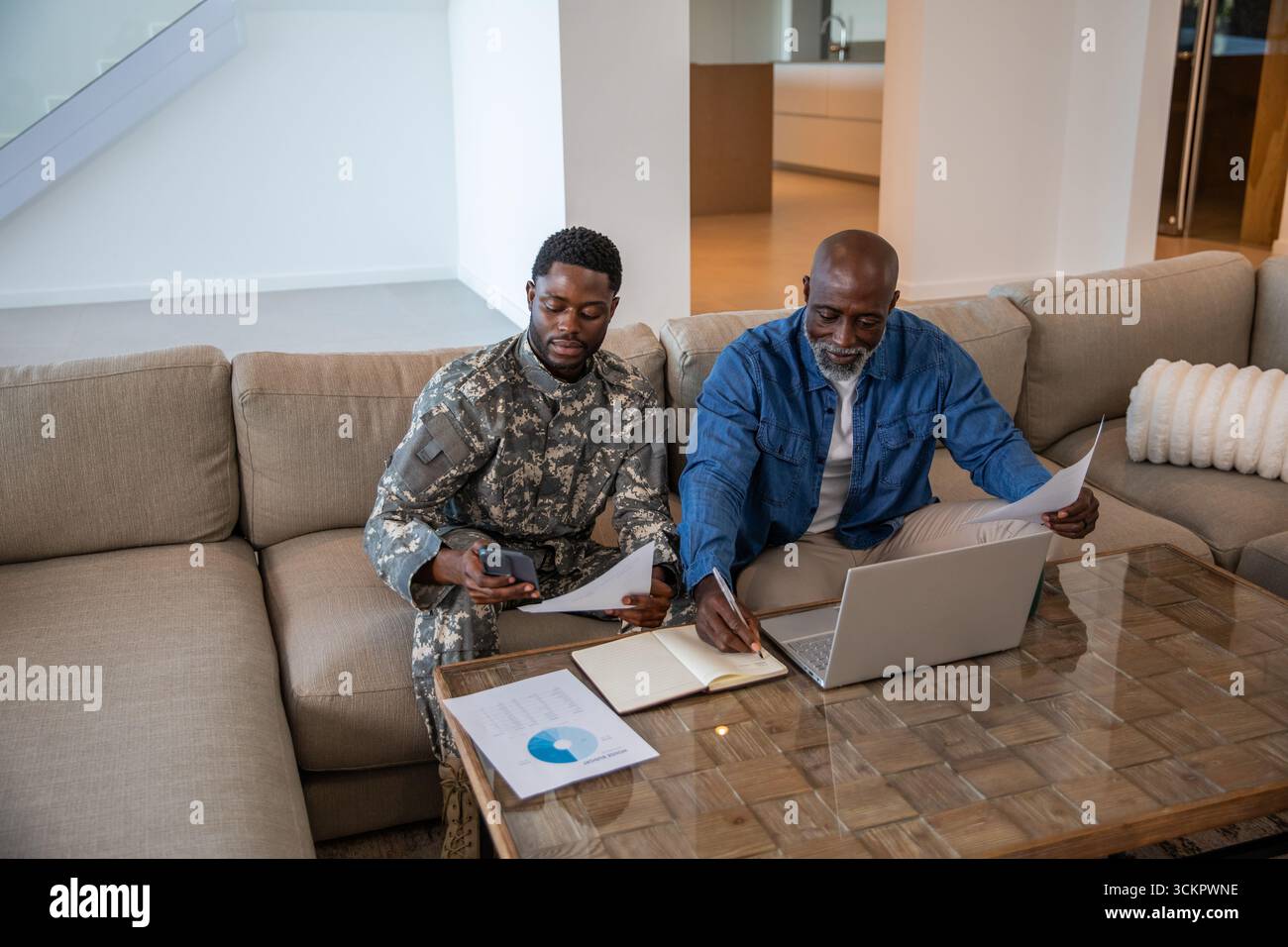 Père et fils afro-américains portant un uniforme camouflage examinant des rapports sur une table basse à la maison Banque D'Images