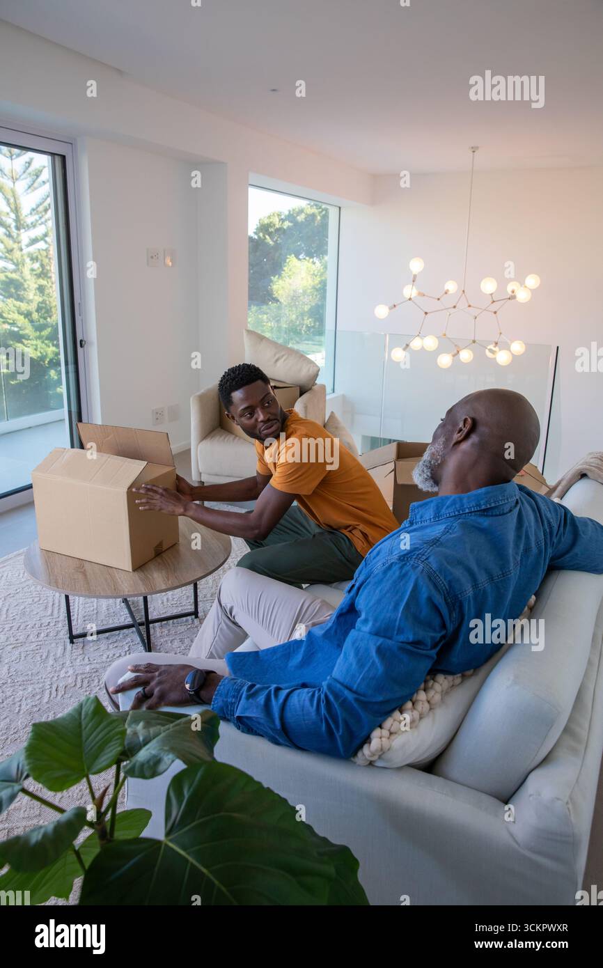 Père afro-américain et fils déballant la boîte en carton sur la table basse ronde dans le salon Banque D'Images Père afro-américain et fils déballant la boîte en carton sur la table basse ronde dans le salon Banque D'Images