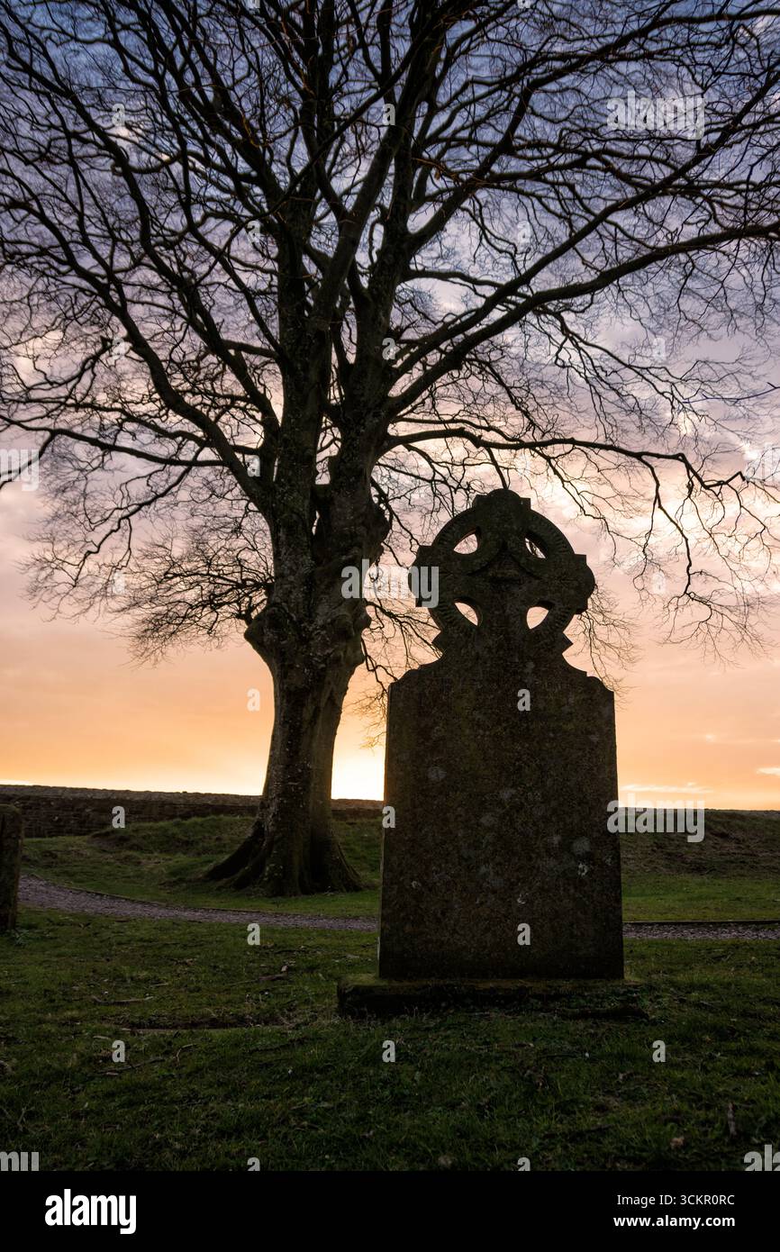 Ancienne pierre tombale de croix celtique silhouette au coucher du soleil Banque D'Images