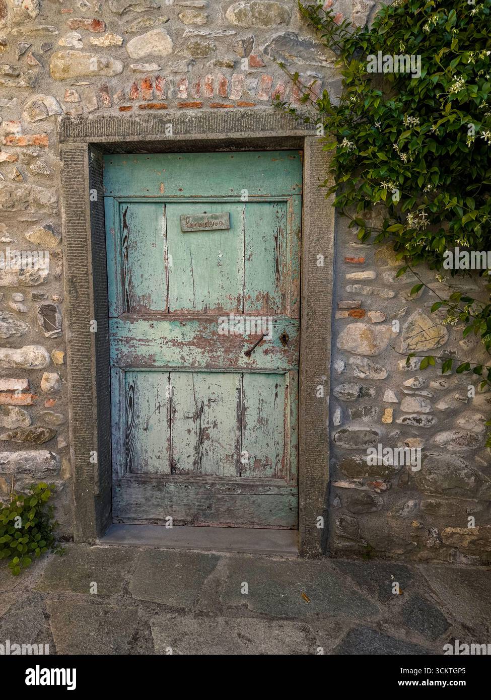 Une vieille porte en bois lourde avec peinture décolorée et pelable, attachée à un ancien moulin à eau en Toscane, Italie Banque D'Images
