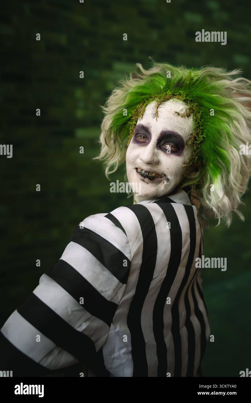 Gros plan portrait d'un jeune cosplayer masculin riant et s'amusant habillé en Beetlejuice avec de la peinture pour le visage et des cheveux verts Banque D'Images