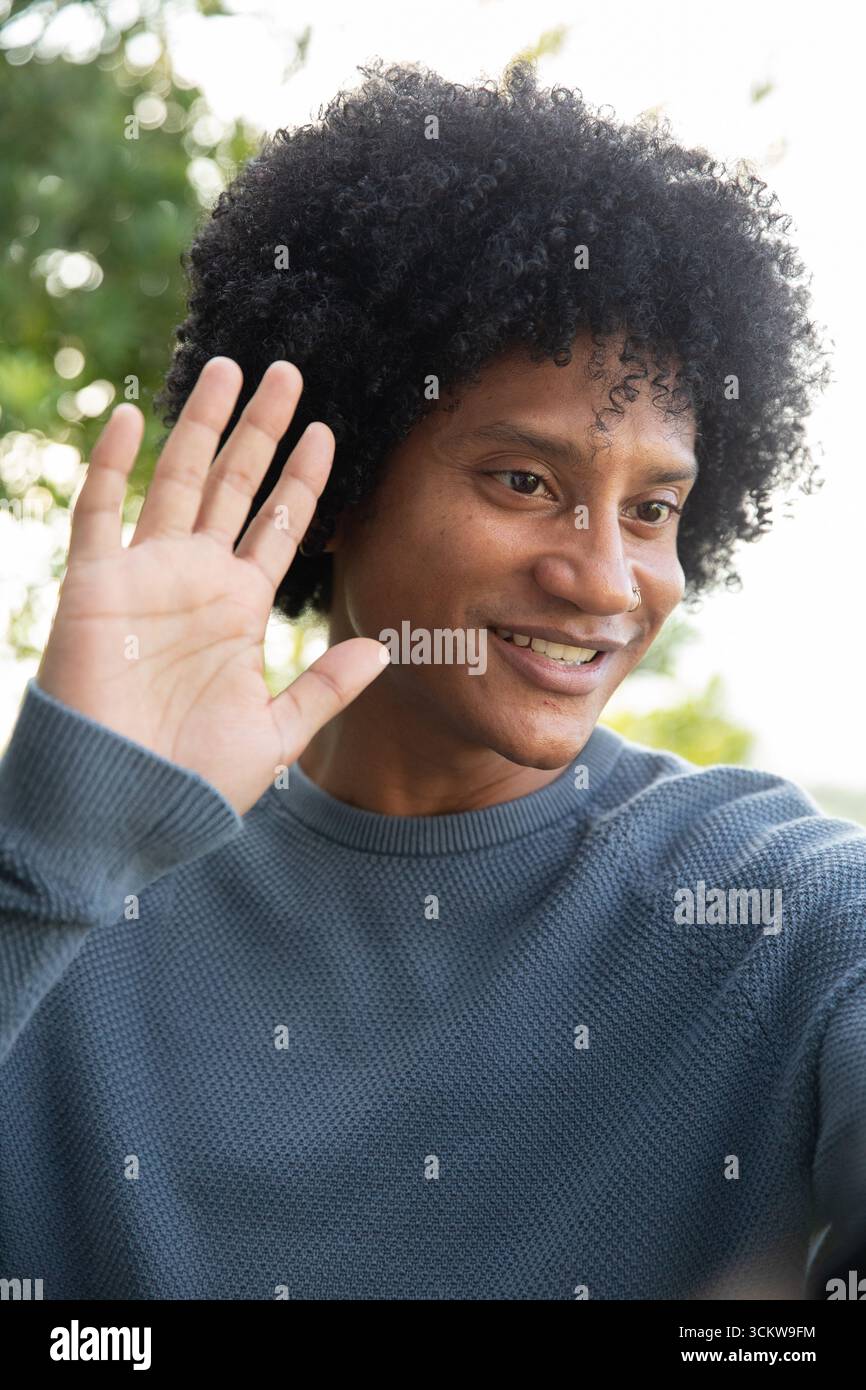 Homme afro-américain agitant la main dans le jardin en pull bleu avec anneau de nez Banque D'Images Homme afro-américain agitant la main dans le jardin en pull bleu avec anneau de nez Banque D'Images