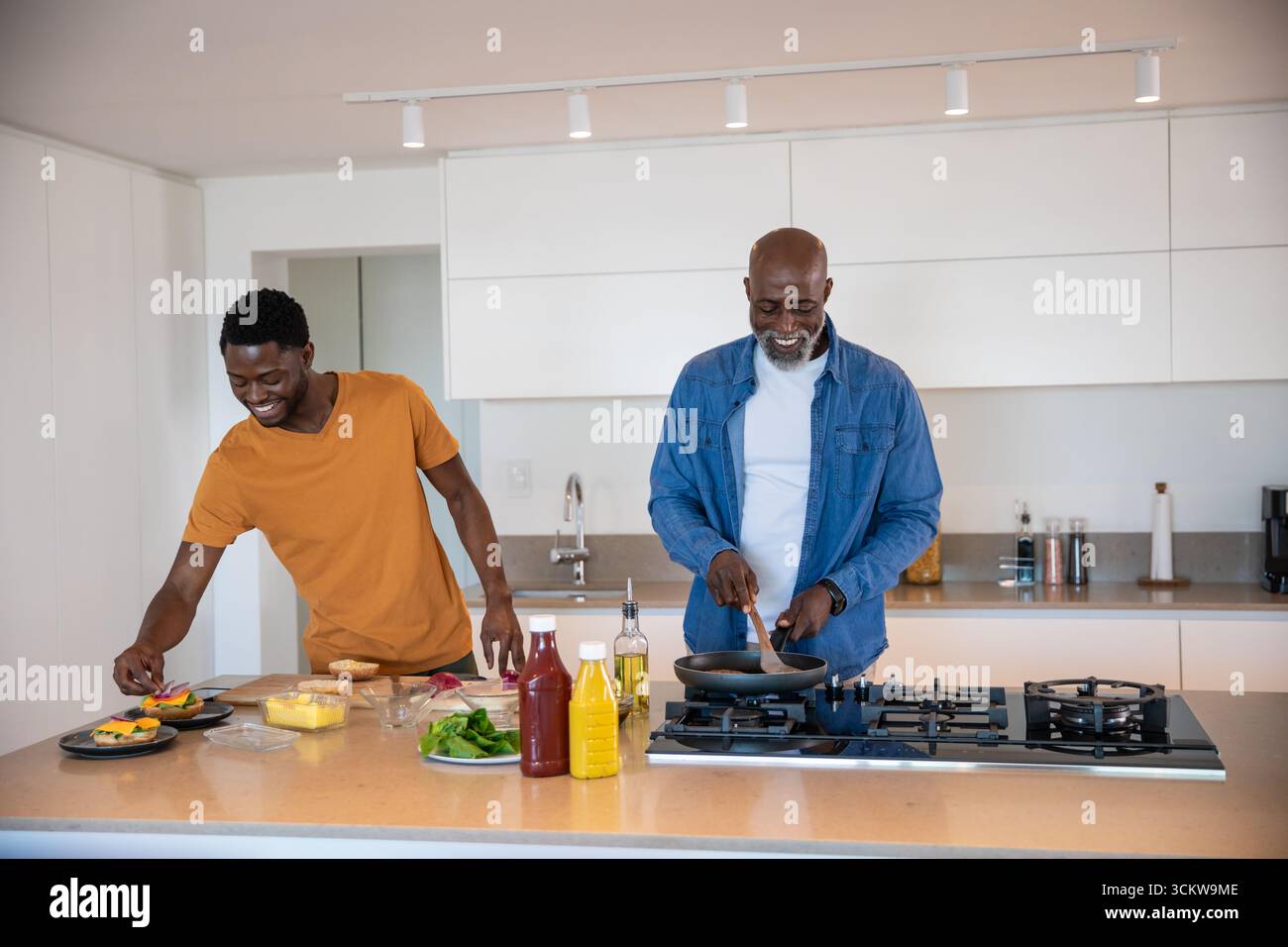 Père afro-américain, fils remuant dans une poêle à frire, disposant des légumes sur des assiettes dans la cuisine Banque D'Images Père afro-américain, fils remuant dans une poêle à frire, disposant des légumes sur des assiettes dans la cuisine Banque D'Images