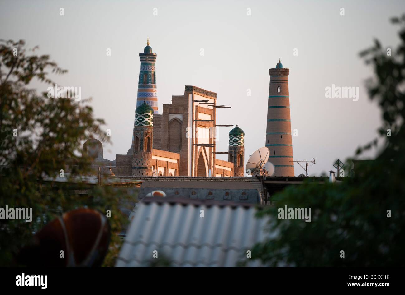 Une antenne parabolique et des minarets avec madrassa reflètent la lumière de fin de soirée dans la vieille ville de Khiva, en Ouzbékistan. Banque D'Images