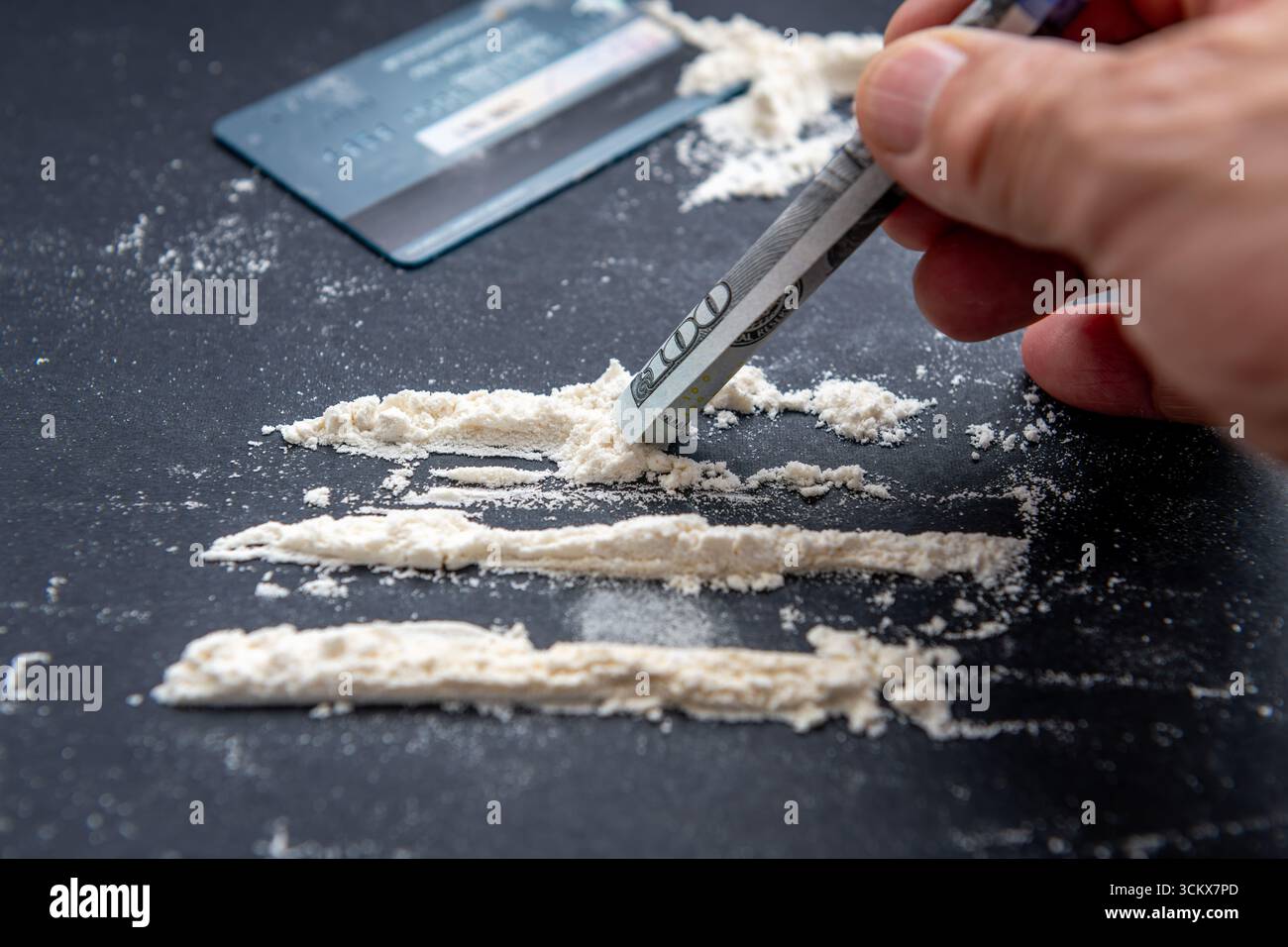 Un concept de prise de drogue illicite, de dépendance avec une personne utilisant un billet d'un dollar américain roulé pour aspirer des rangées de farine blanche ordinaire. Banque D'Images