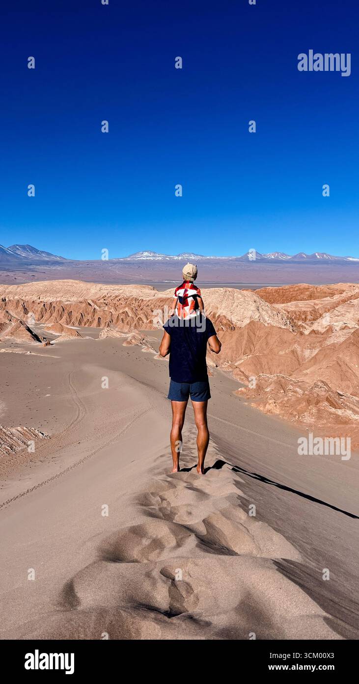 Photo verticale d'un touriste méconnaissable tenant son fils ou son tout-petit sur les épaules, tout en se tenant debout au sommet de la dune et en regardant Licancabur Banque D'Images Photo verticale d'un touriste méconnaissable tenant son fils ou son tout-petit sur les épaules, tout en se tenant debout au sommet de la dune et en regardant Licancabur Banque D'Images