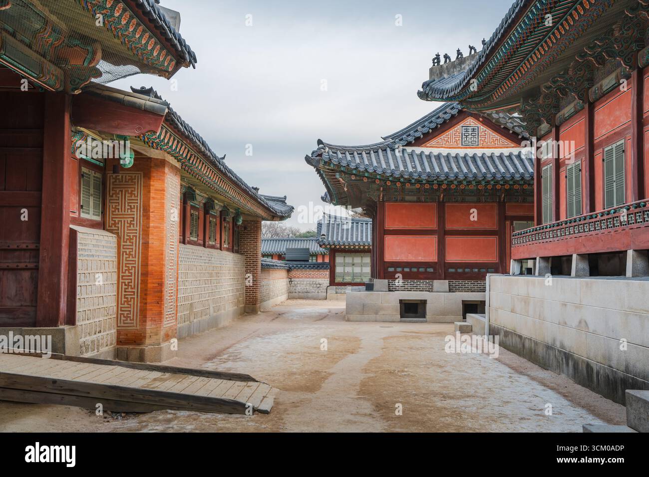 Vue détaillée de la cour du palais de Gyeongbokgung à Séoul avec des toits de tuiles ornées, des murs en bois rouge et des motifs dancheong complexes. Banque D'Images