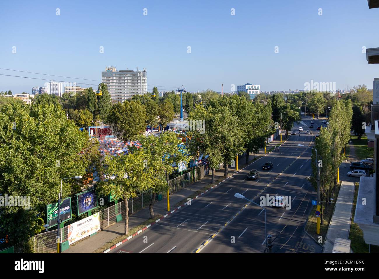 Vue surélevée d'une rue urbaine bordée d'arbres verts, de bâtiments modernes et de téléphériques au-dessus. Banque D'Images