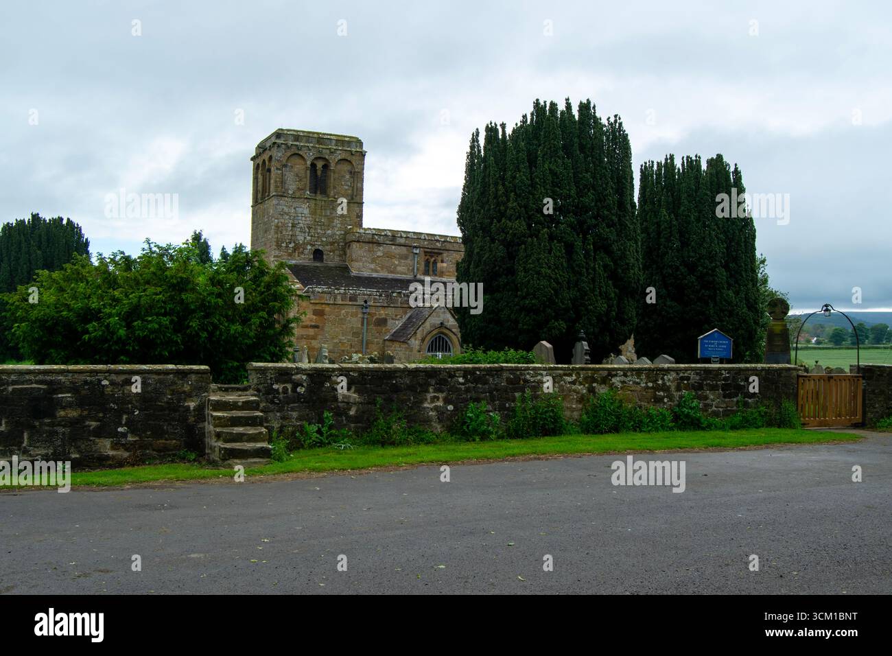 L'église Marie la Vierge, Leake, près de Thirsk, se dresse grandiose derrière un mur de pierre et des cyprès sous un ciel nuageux et atmosphérique. Banque D'Images