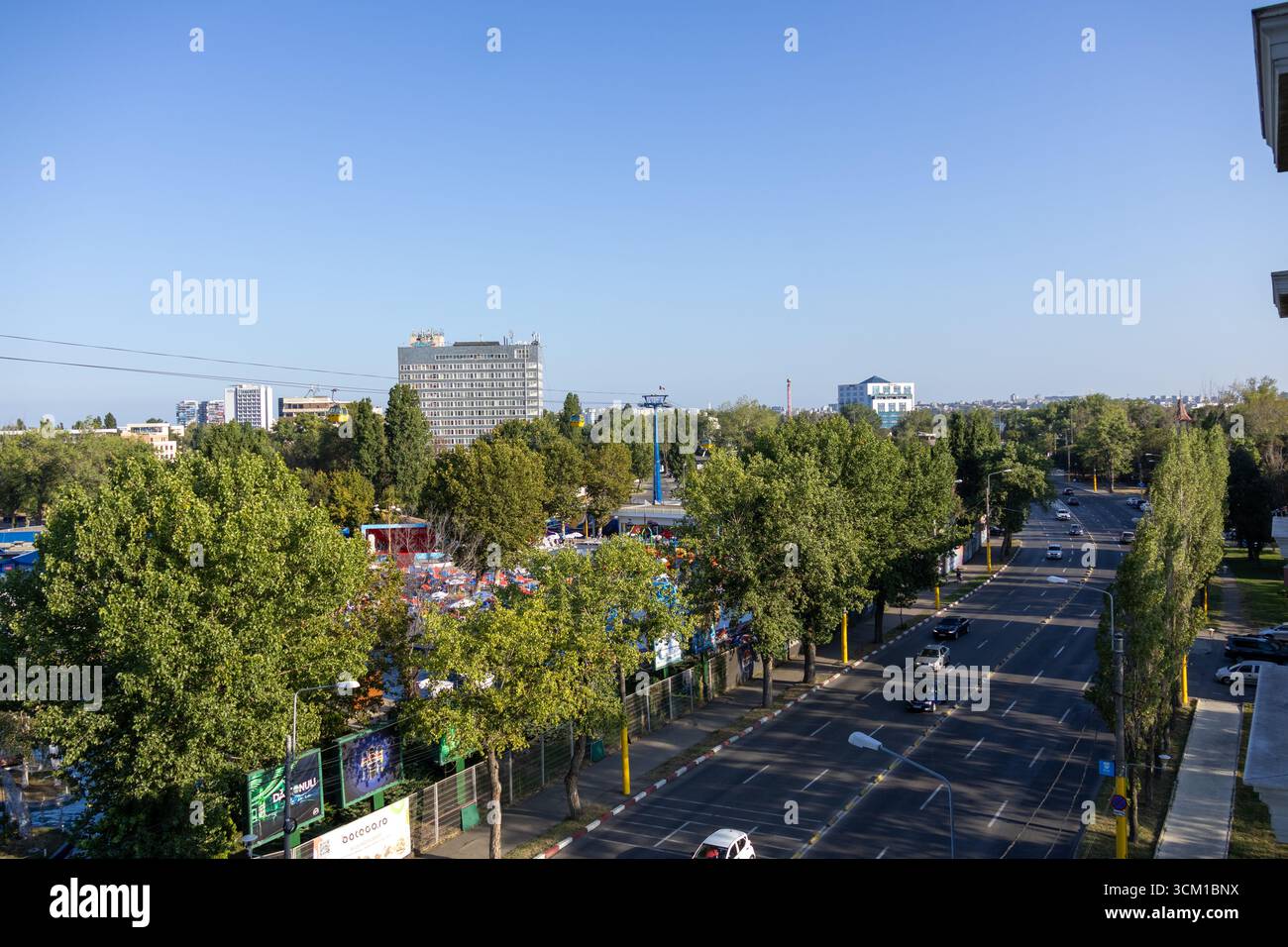 Vue surélevée d'une rue urbaine bordée d'arbres verts, de bâtiments modernes et de téléphériques au-dessus. Banque D'Images