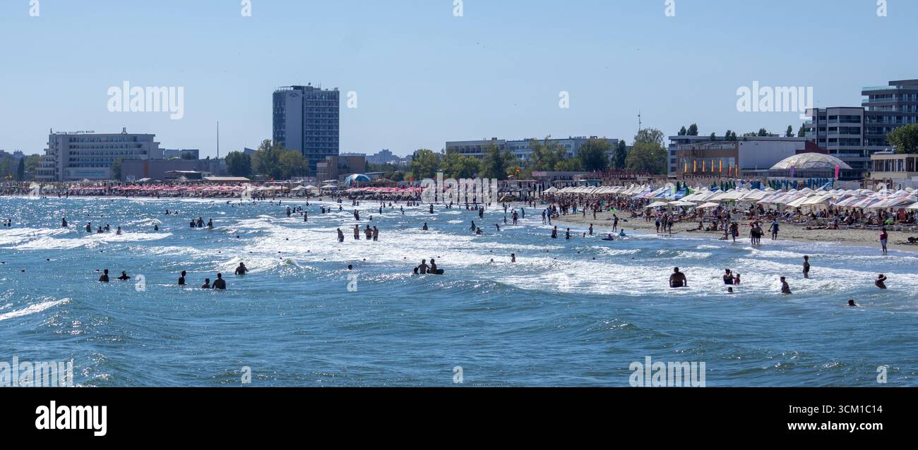 Scène de plage d'été animée avec des touristes nageant dans la mer, se relaxant sur le sable, et des hôtels en arrière-plan Banque D'Images