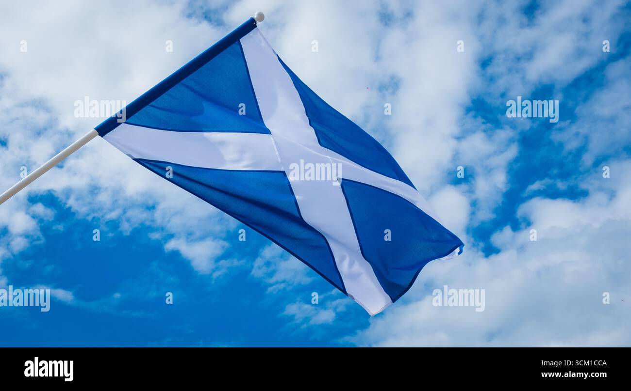 Le drapeau national de l’Écosse, le Saltire ou encore la Croix d’Andrew, volant sur un mât de drapeau contre un ciel bleu aux nuages éparpillés, symbolisant l’écossais Banque D'Images