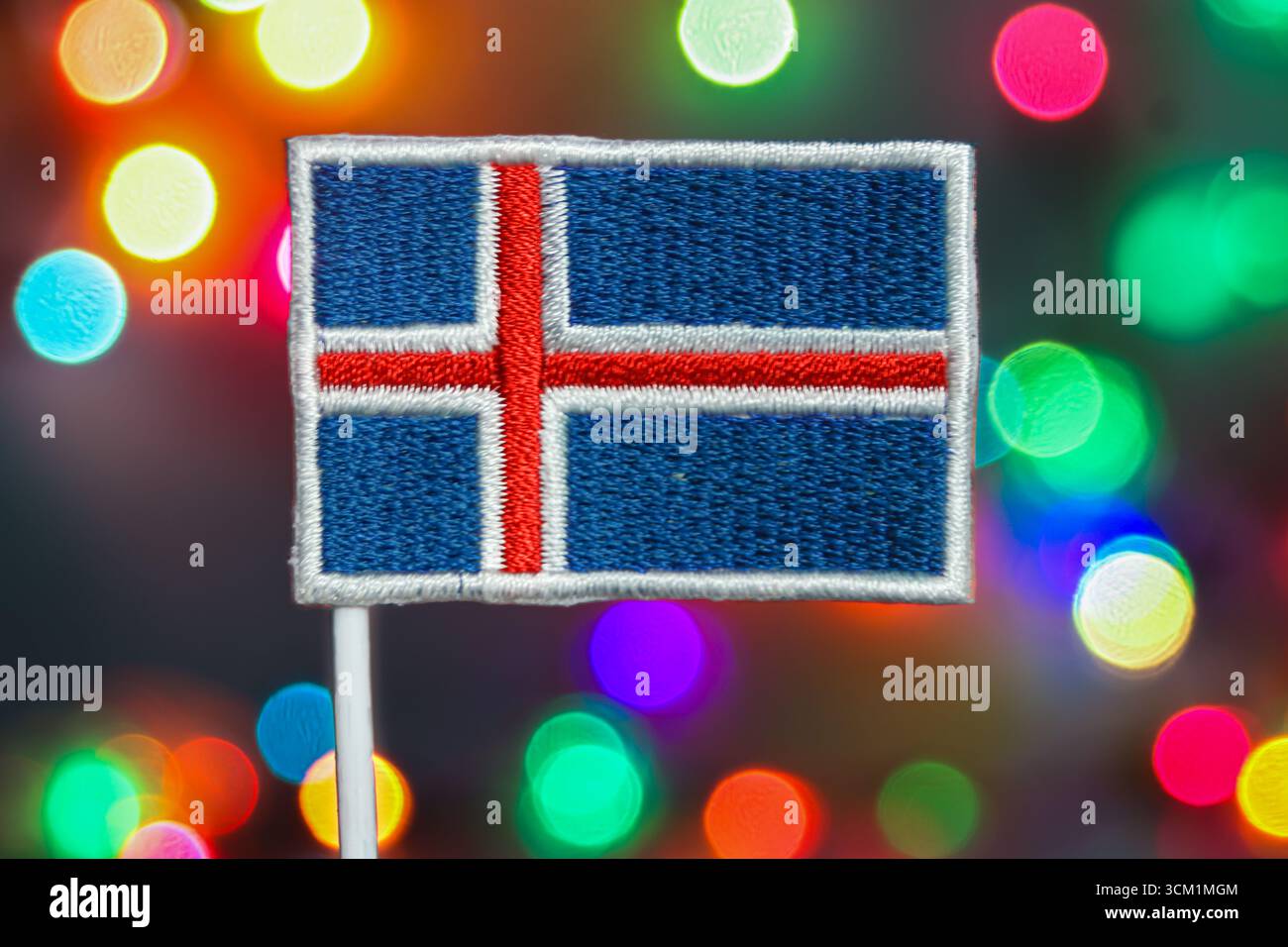 Broderie de drapeau islandais devant des lumières bokeh colorées, lueur festive symbolisant les feux d'artifice, la célébration du nouvel an et l'esprit des vacances de Noël. Banque D'Images