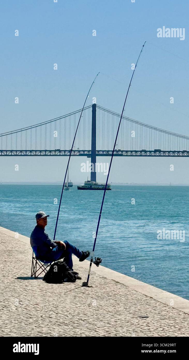 Pêcheur mâle pêchant sur la rive du Tage Lisbonne avec Ponte 25 de Abril en arrière-plan - Image de stock capturée avec un smartphone