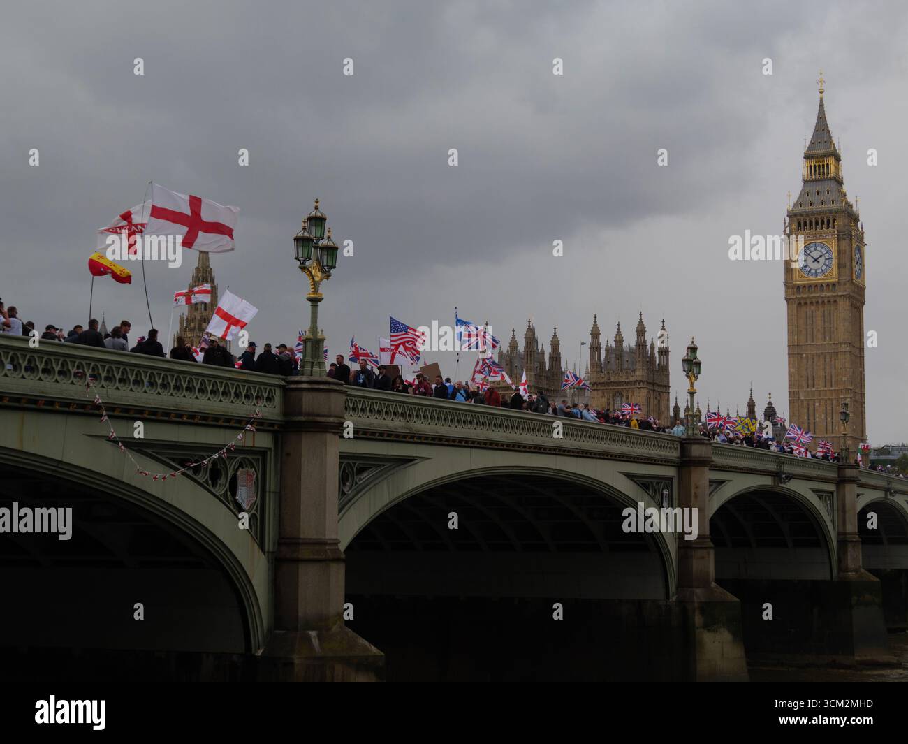 Manifestation unite the Kingdom, 13 septembre 2025, Westminster, Londres, Royaume-Uni. Sous des nuages sombres, des manifestants arborant les drapeaux de l'Union Jack et de St George défilent à travers Westminster Bridge, dans le centre de Londres, lors d'une manifestation organisée par Tommy Robinson, avec Big Ben en arrière-plan Banque D'Images