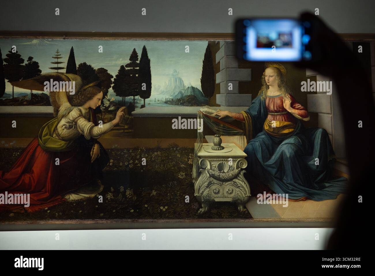 Visiteurs photographiant la peinture « Annonciation » de Léonard de Vinci avec des smartphones modernes dans la Galerie des Offices, Florence, Italie, mettant en valeur l’art, le culte Banque D'Images