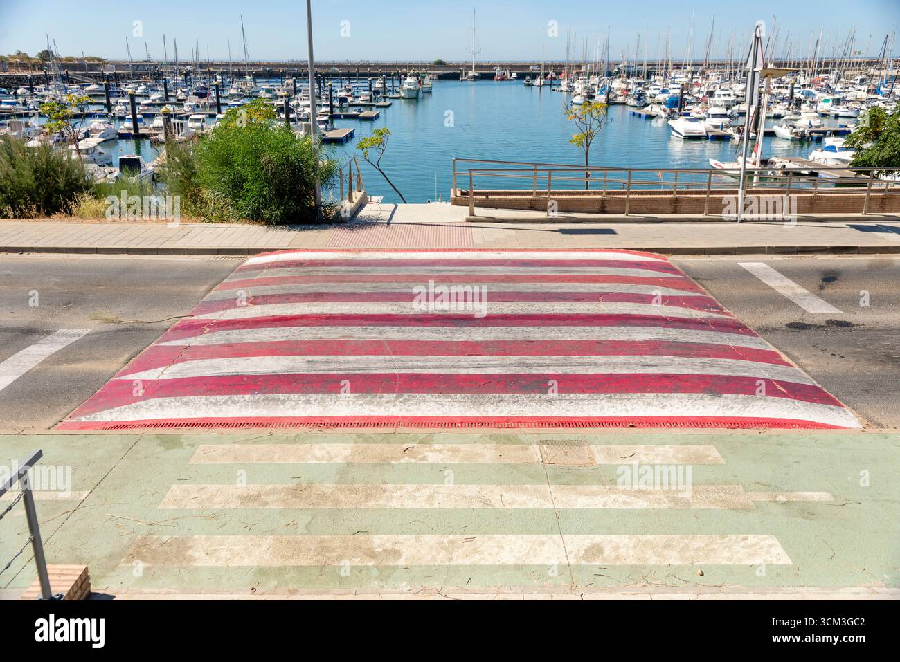 Vista desde un paso de cebra del Puerto deportivo, varios tipos de barcos en sus amarres, en dia soleado con Agua tranquila y el espigon que les rodea Banque D'Images