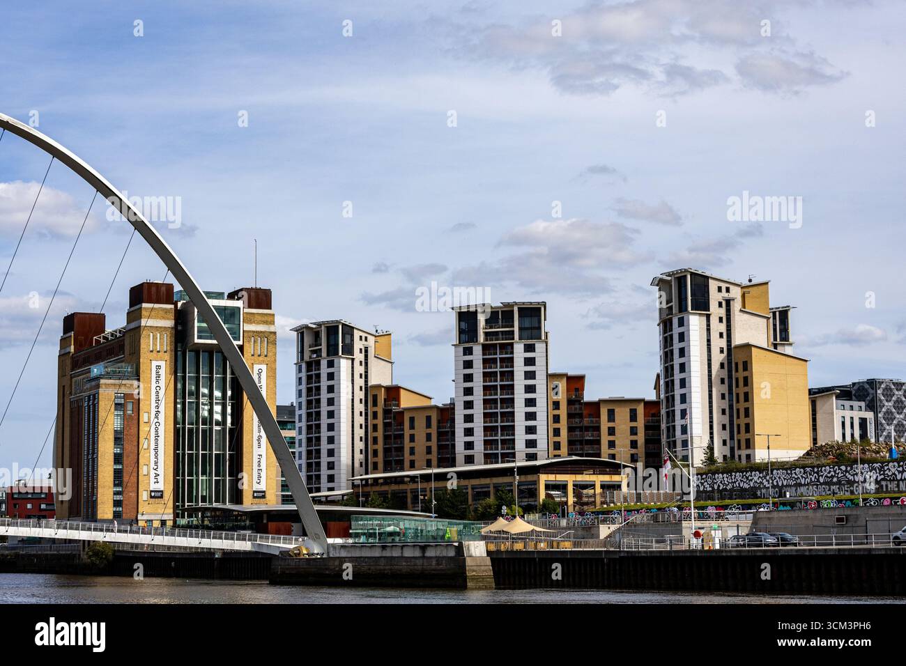 Un paysage urbain moderne dispose d'un grand pont voûté au premier plan, avec une rivière et divers bâtiments en arrière-plan sous un ciel nuageux à newca Banque D'Images