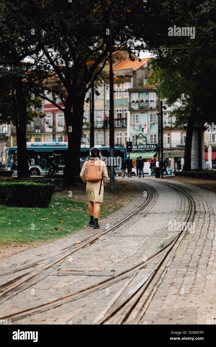 Personne marchant le long des pistes de tramway courbes dans un parc urbain verdoyant à Porto, Portugal. Balade en ville d'automne, européenne, chemin pavé, voyageur sac à dos Banque D'Images