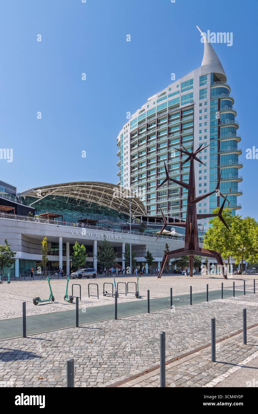 Le bâtiment Vasco da Gama et une statue unique se dressent sur une place pavée du Parque das Nações à Lisbonne. Deux scooters électriques verts sont garés à proximité. Lisb Banque D'Images