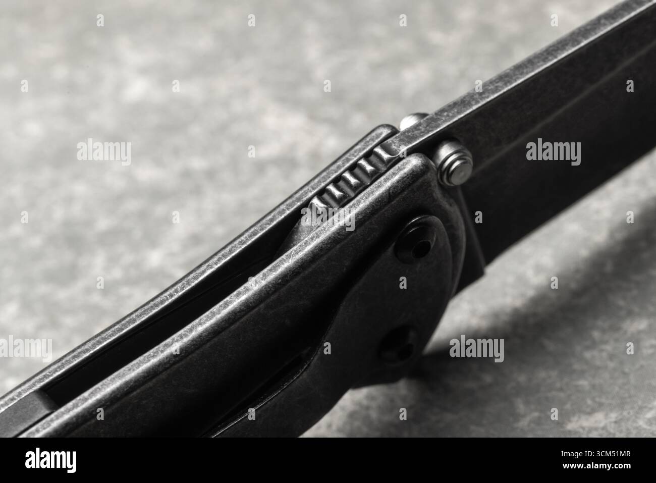 Macro photo détaillée d'un couteau pliant noir moderne avec poignée texturée et charnière visible, placé sur un fond gris, mettant en valeur sa durabilité et p Banque D'Images