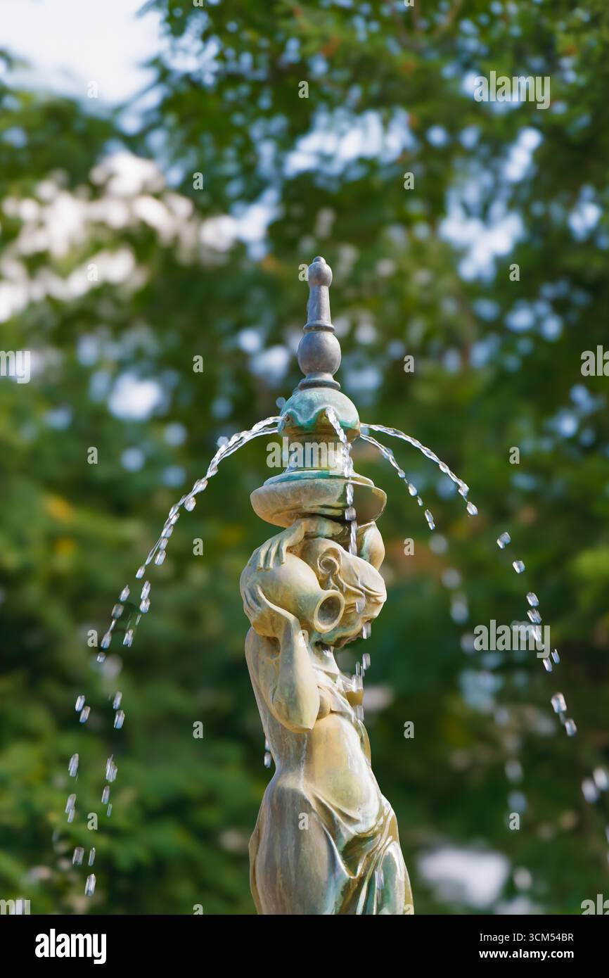 Fontaine artistique en bronze représentant une femme avec une cruche sur l'épaule, versant de l'eau dans l'air. Détail de sculpture décorative dans un parc extérieur vert Banque D'Images