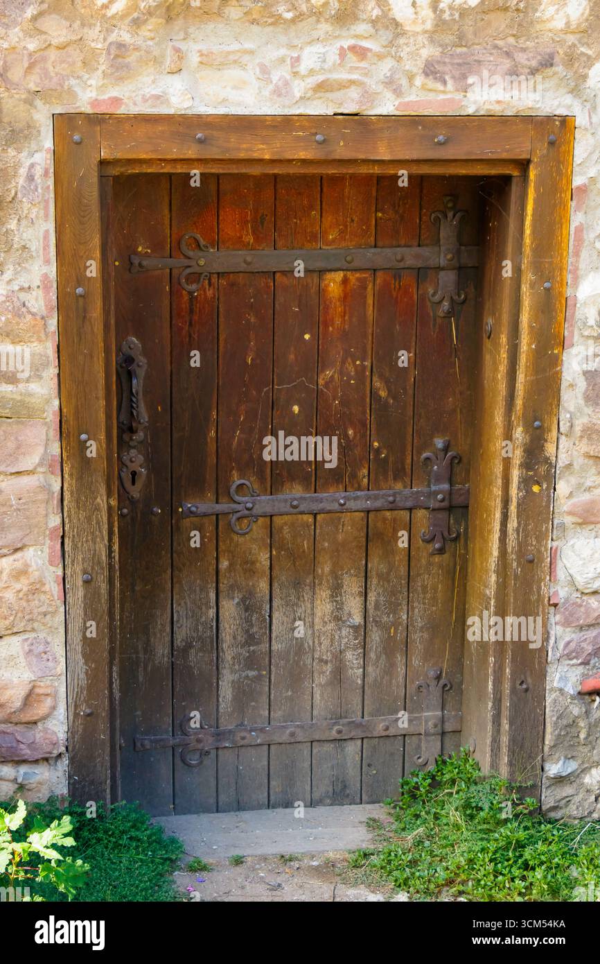 Une porte médiévale en bois robuste avec des charnières en fer ornées et une poignée, encadrée par un mur de pierre antique. L'entrée rustique reflète l'architecture de la forteresse Banque D'Images