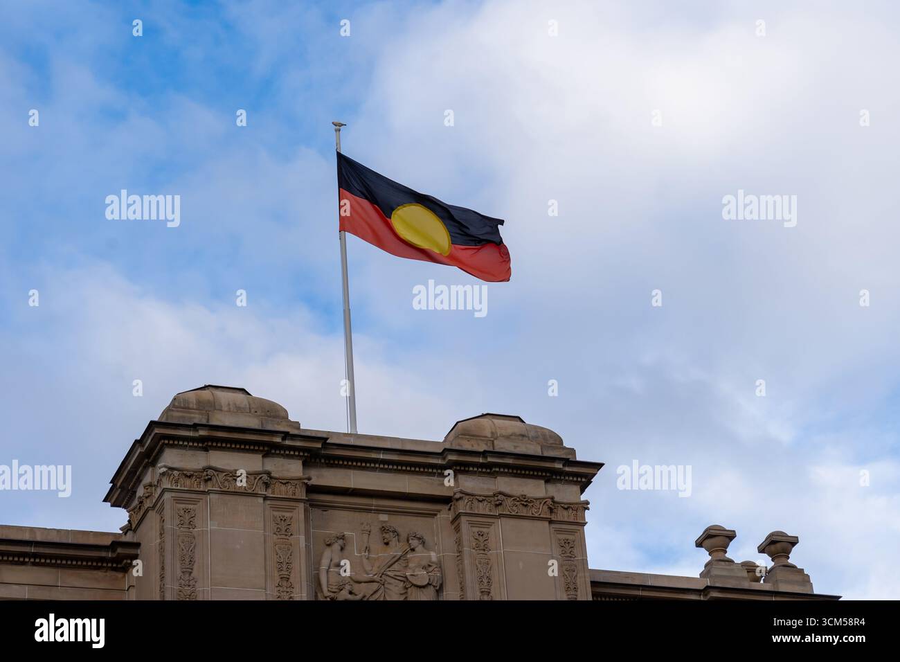 Drapeau des aborigènes australiens agitant sur le bâtiment du Parlement sur Spring Street à Melbourne, Victoria, Australie. Banque D'Images