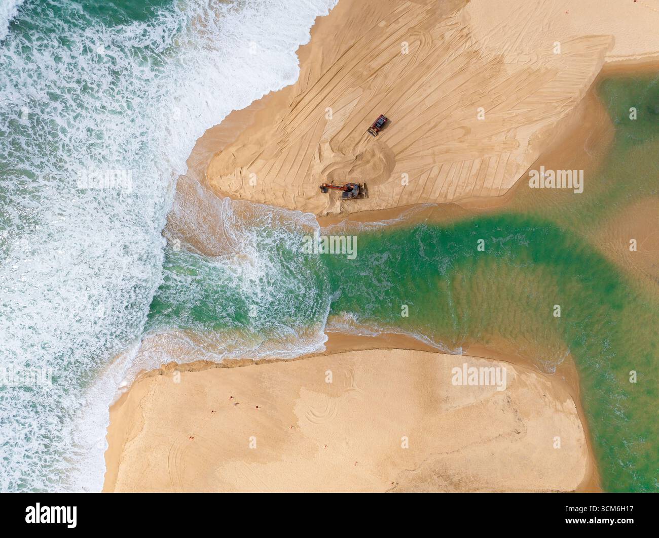 Vue aérienne d'engins de terrassement ouvrant un canal d'eau d'un lac à l'océan à Currimundi sur le Sunshine Caost dans le Queensland, Australie Banque D'Images