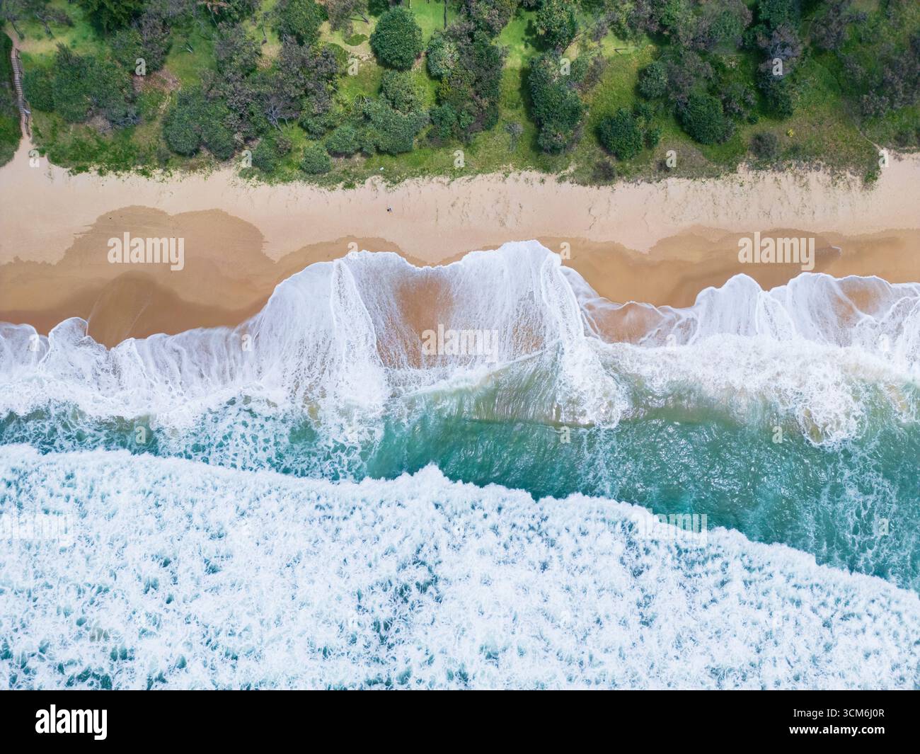 Vue aérienne des vagues sur une plage de sable en face de la végétation côtière à Currimundi sur la Sunshine Coast dans le Queensland, Australie. Banque D'Images