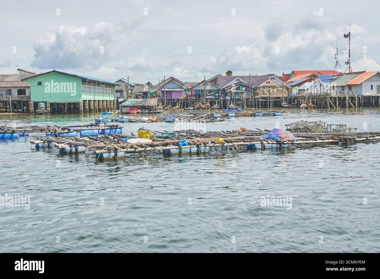 PHUKET, THAÏLANDE - 12 NOVEMBRE 2017 : village de pêcheurs côtier avec maisons sur pilotis et fermes de poissons flottants dans des eaux tranquilles sous ciel nuageux. Banque D'Images