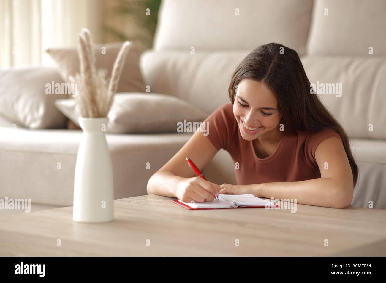 Femme heureuse prenant note dans l'agenda papier assis sur le sol dans le salon Banque D'Images