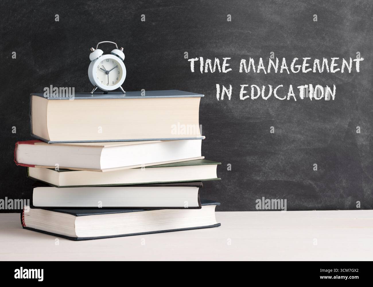 Réveil placé sur une pile de livres avec un tableau noir en arrière-plan avec le texte gestion du temps dans l'éducation écrit dessus Banque D'Images