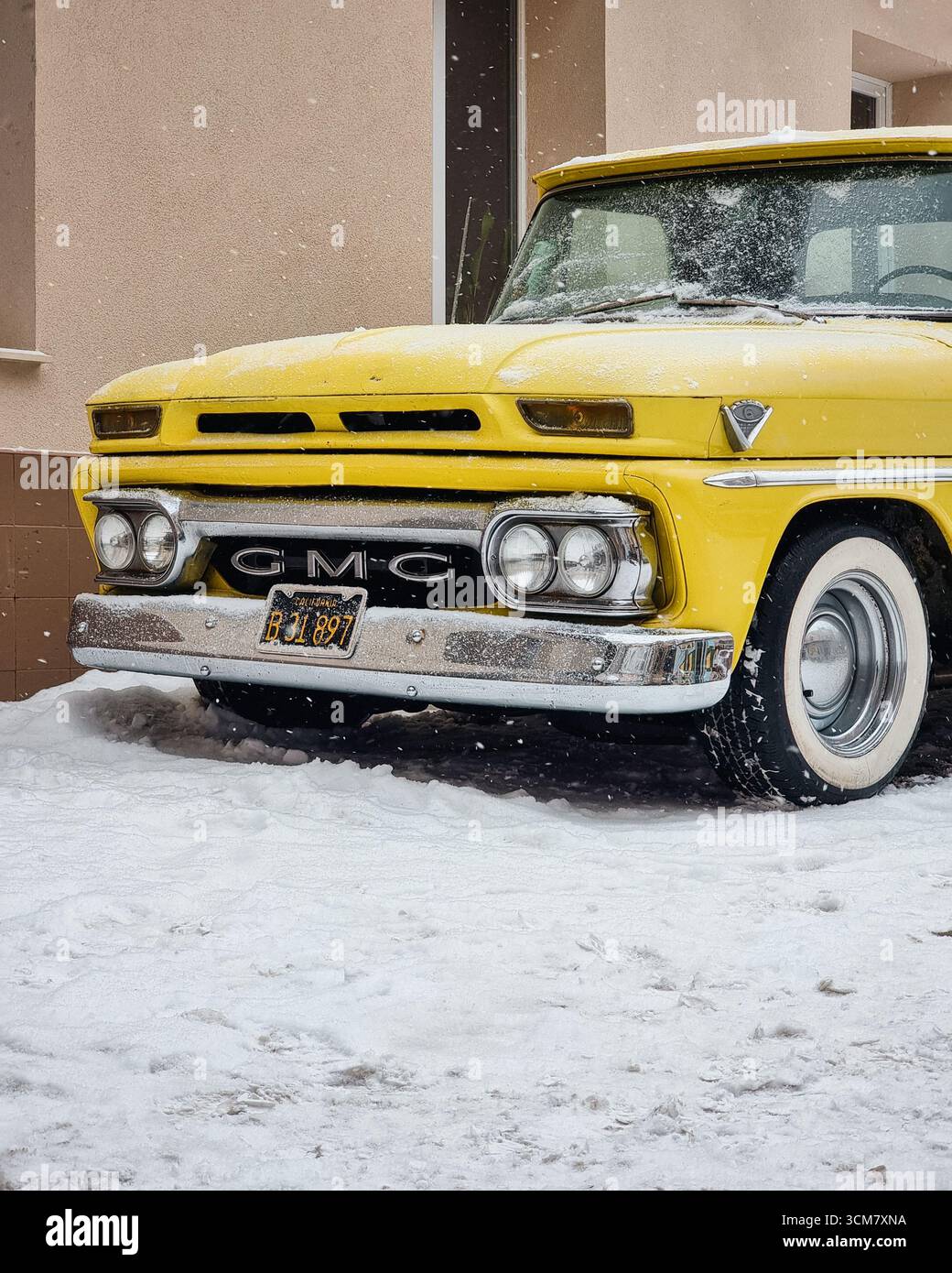 Vieux camion jaune garé près d'un bâtiment beige un matin d'hiver. Partie avant d'un camion GMC 1000 1965 dans une cour enneigée. Banque D'Images