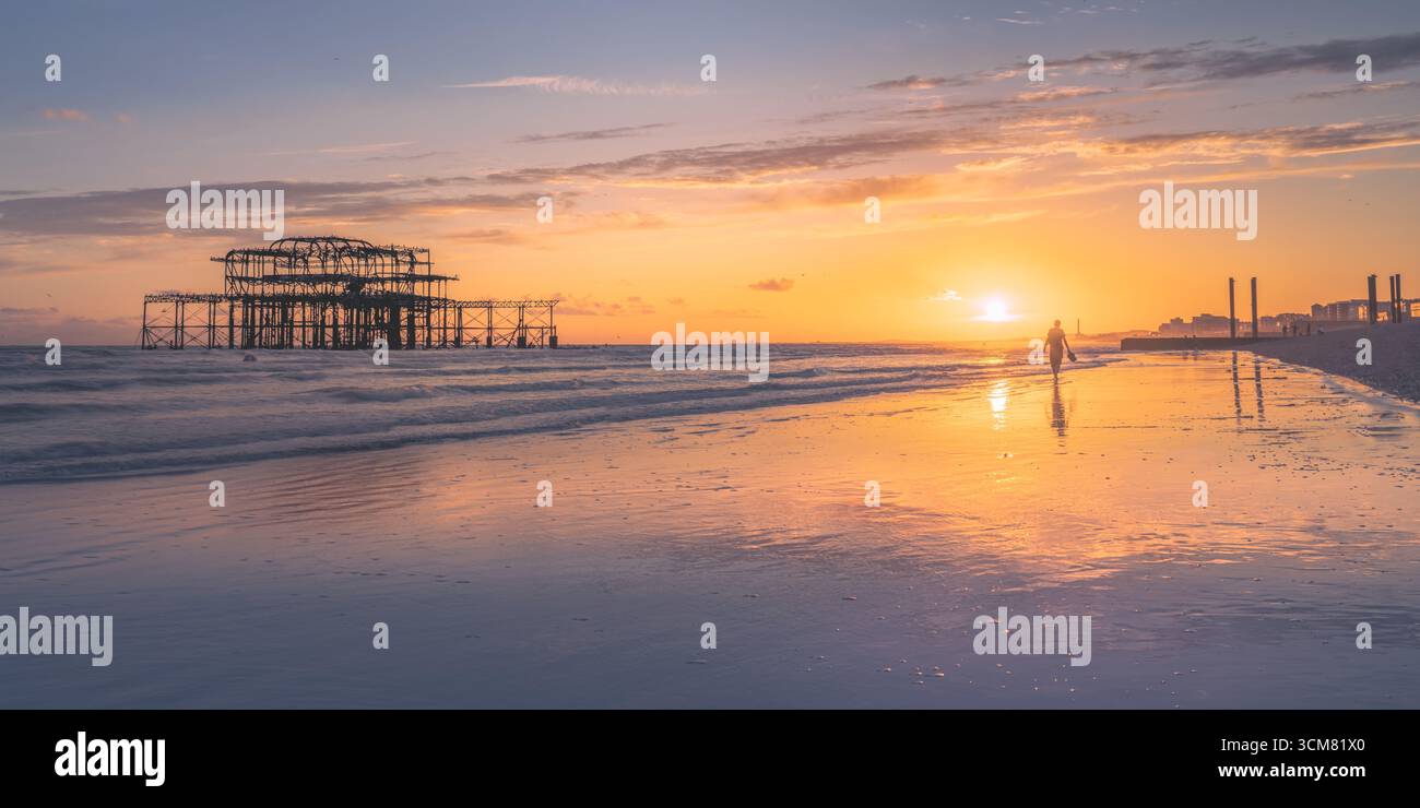 Silhouette de personne marchant sur la plage de Brighton au coucher du soleil avec les ruines de West Pier, East Sussex, Angleterre Banque D'Images