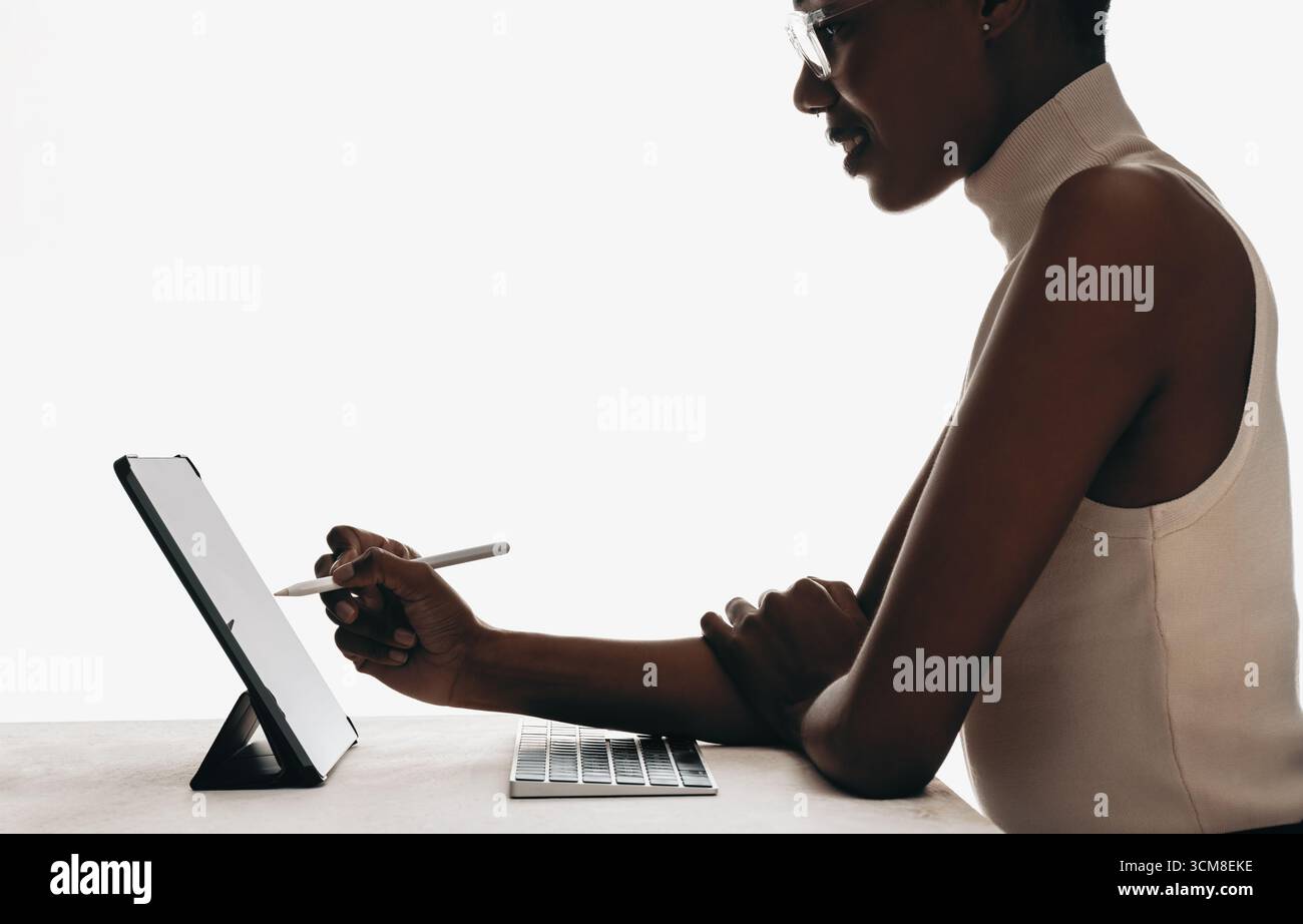 Un professionnel utilise une tablette avec un stylet, assis à un bureau dans un cadre minimaliste, illustrant l'utilisation de la technologie moderne et le lieu de travail Banque D'Images