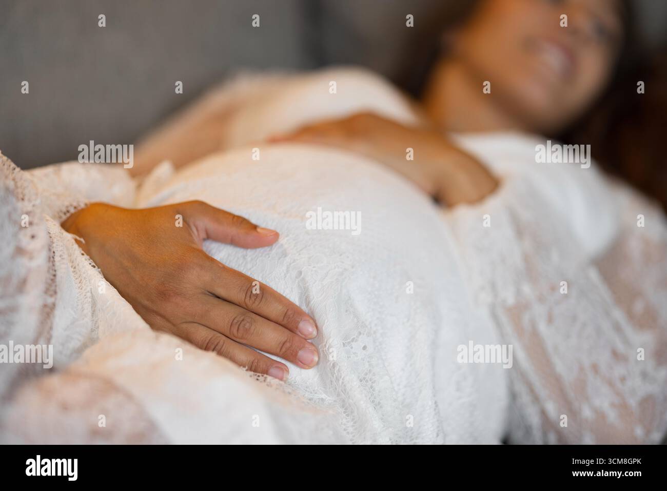 Une image sereine en gros plan d'une femme enceinte portant une dentelle blanche délicate, posant doucement ses mains sur son ventre, symbolisant l'amour maternel, l'anticipation Banque D'Images